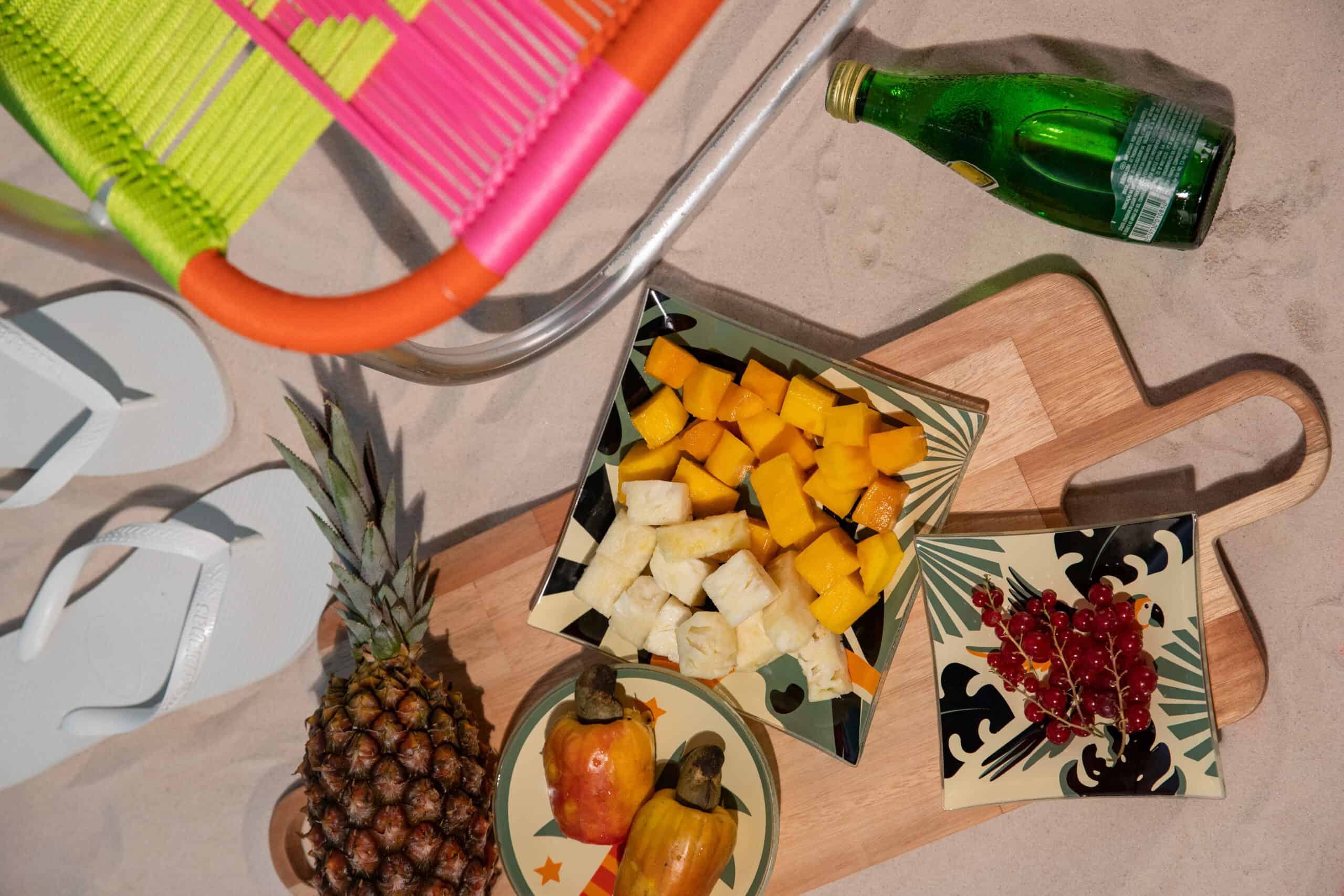 uma bandeja com alimentos típicos do verão: abacaxi, caju e manga. Bem colorida, a decoração conta também com uma garrafa de água