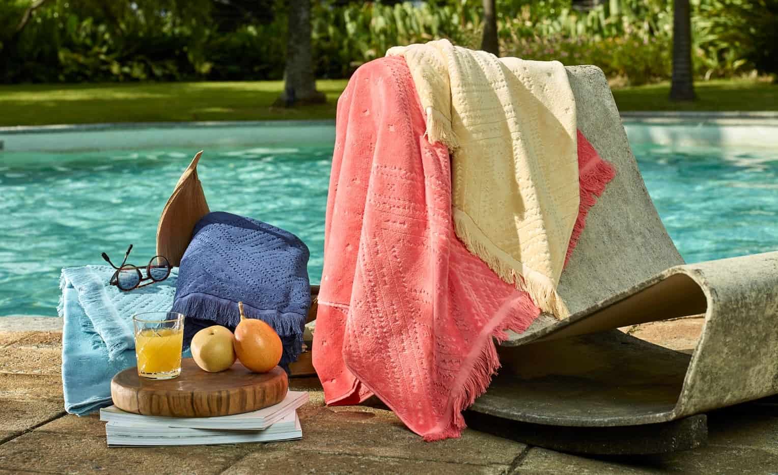 toalhas de praia em uma cadeira a beira de uma piscina, ao lado um copo com suco laranja e duas pêras