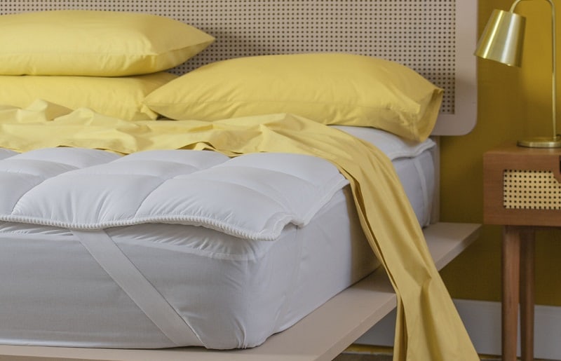 pillow top branco posicionado acima do colchão com lençóis amarelos forrados 