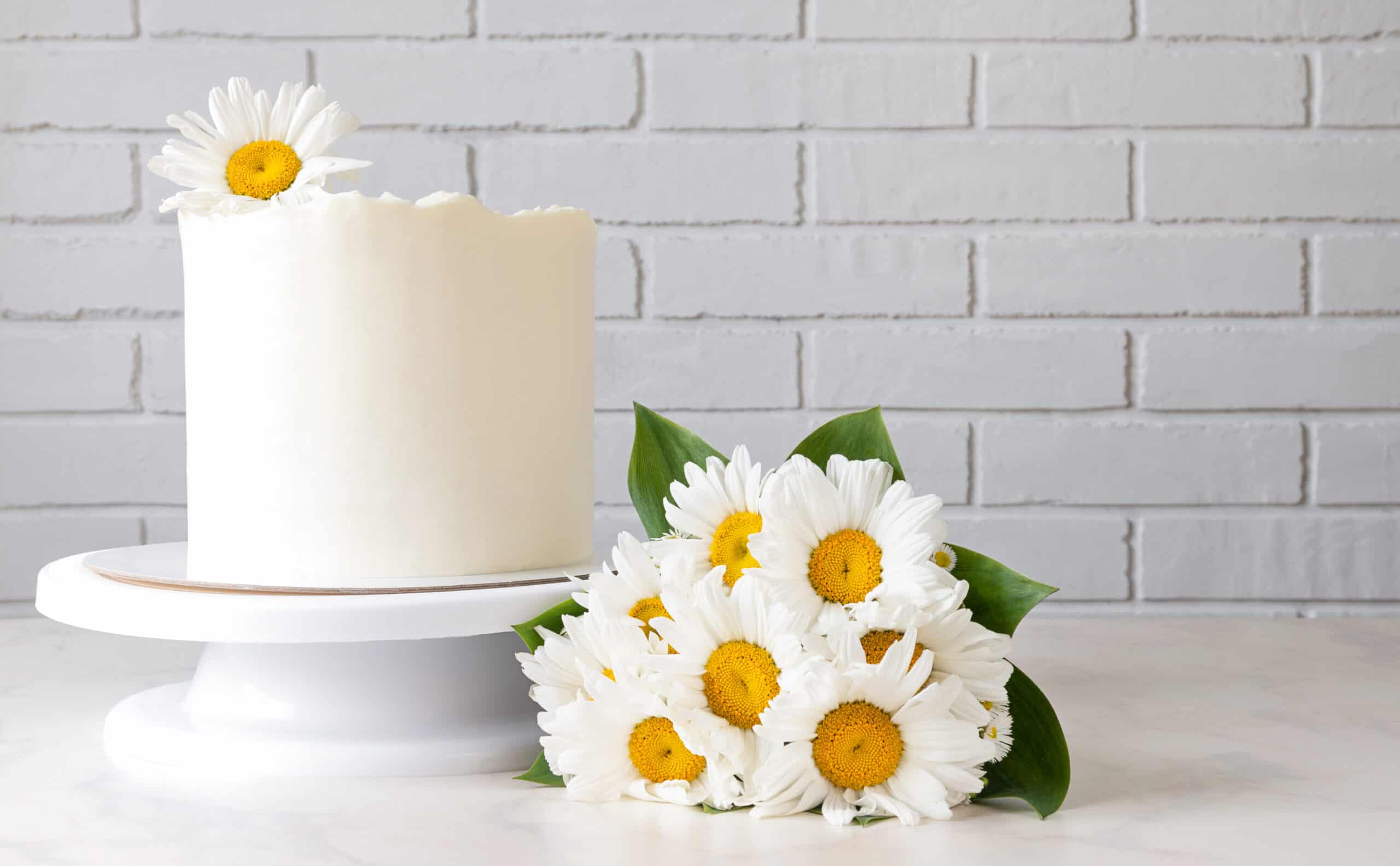 um bolo branco com uma margarida no topo e algumas flores na lateral