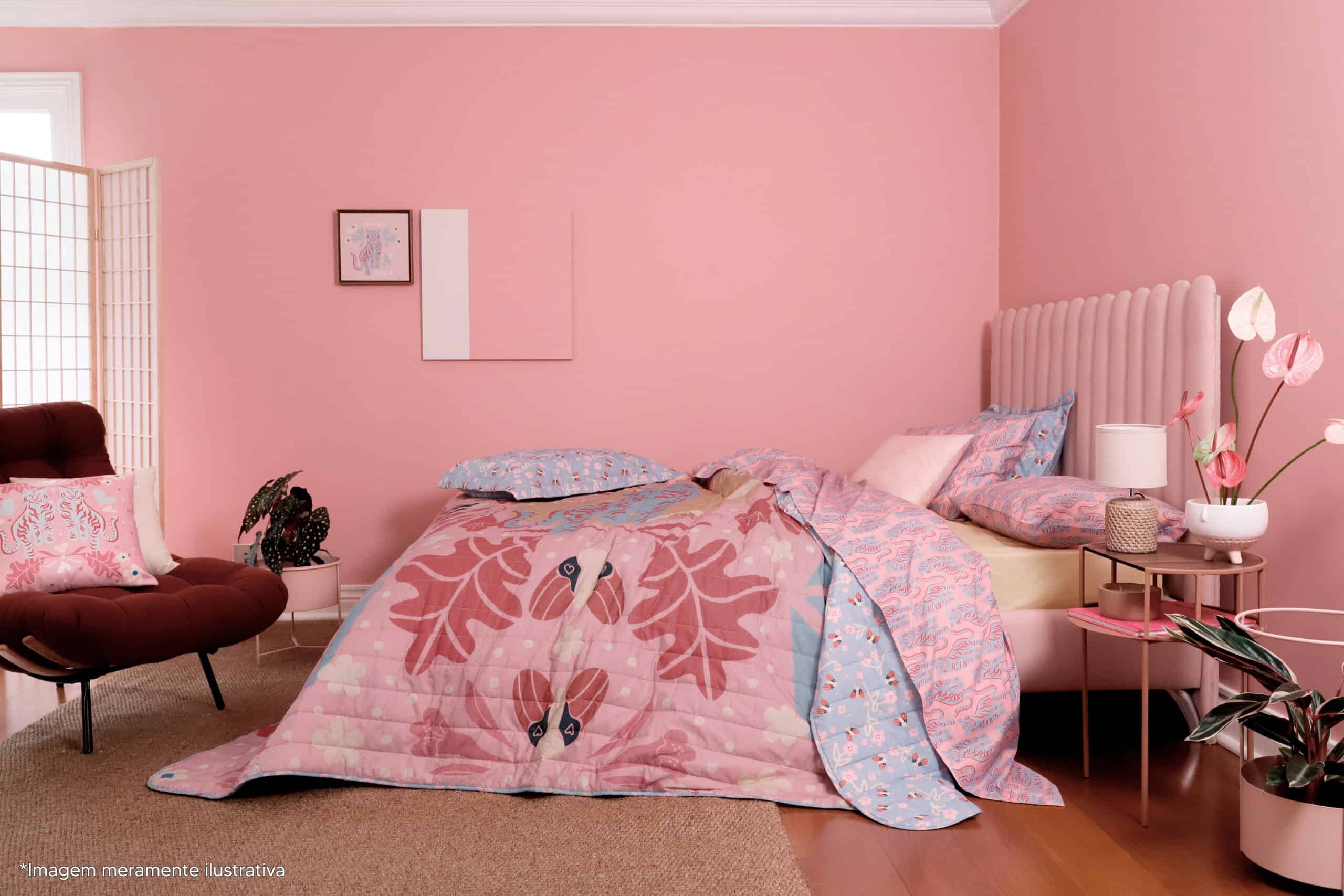 um quarto rosa com uma estampa de cama em tons de rosa e azul e uma estampa exclusiva da coleção Juntas ARTEX. Tem uma planta e dois quadros na parede de fundo